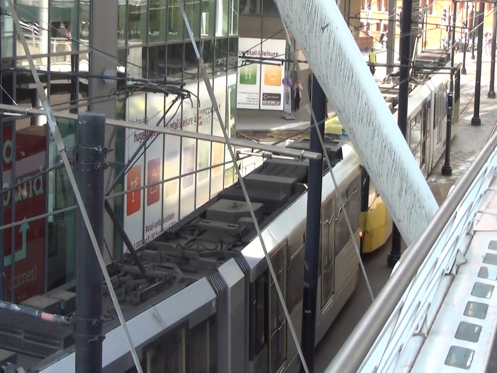 A Metrolink tram at Piccadilly Station, passing under some temporary scaffolding where work is being done.